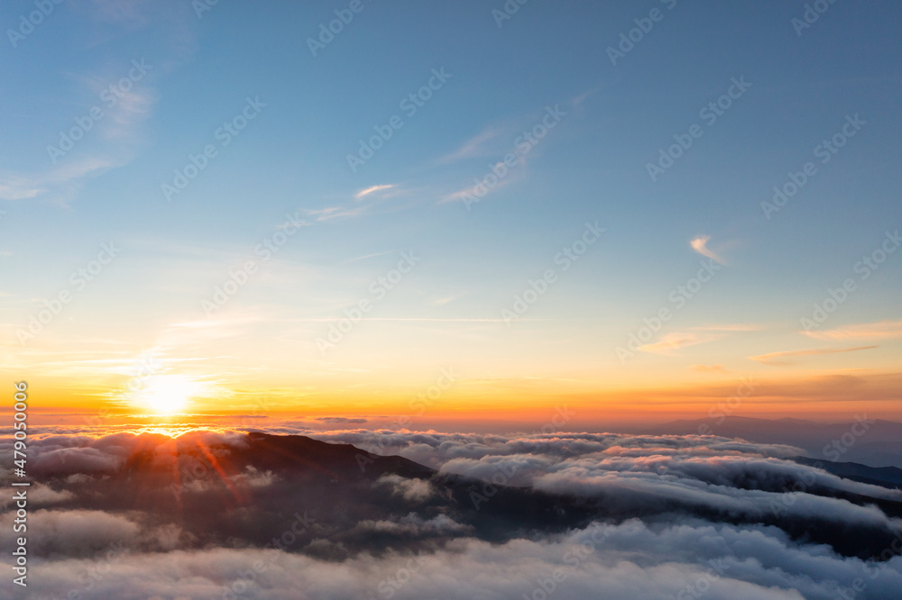 Sun shining above layer of white fluffy clouds at sunset