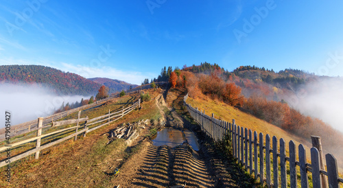 Fototapeta Naklejka Na Ścianę i Meble -  The dirt road is fenced with an old wooden fence. morning mountain landscape.