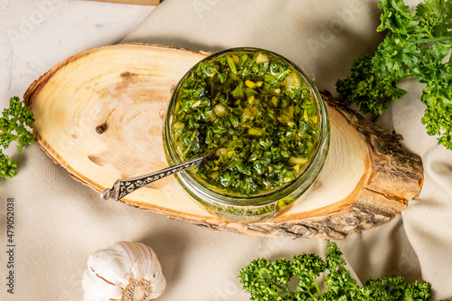 Delicious and healthy chimichurri sauce in a glass jar based on parsley and olive oil on a wooden board, top view. photo