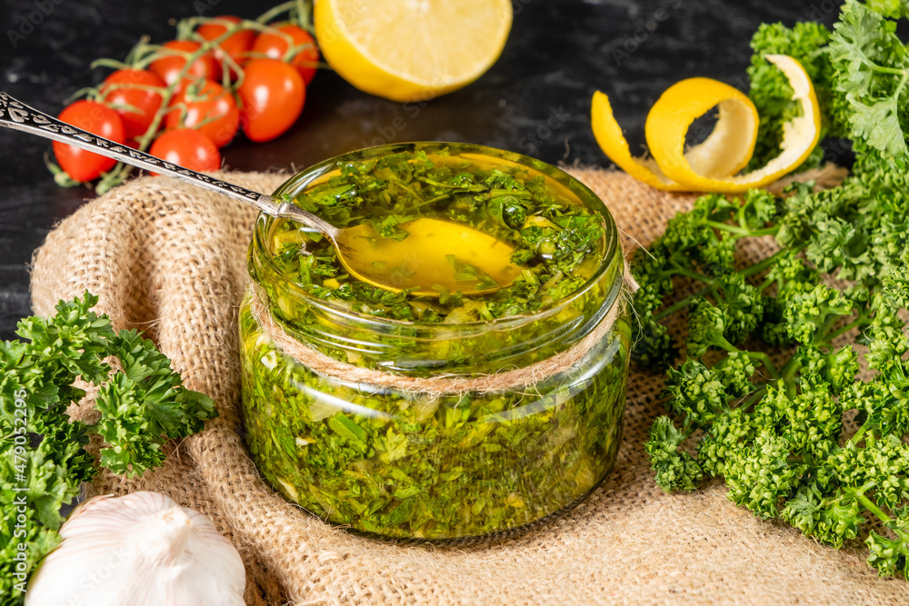 Bright green homemade chimichurri sauce in a glass jar with a spoon. Bright green homemade chimichurri sauce in a glass jar with a spoon.