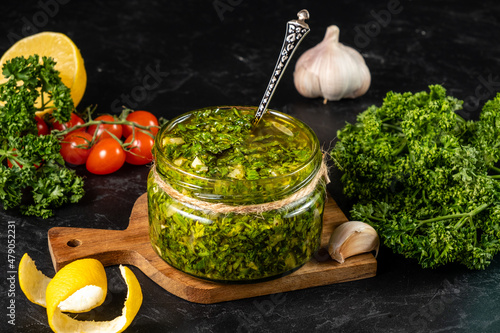 Classic chimichurri sauce based on parsley and olive oil in a transparent jar on a dark table. photo