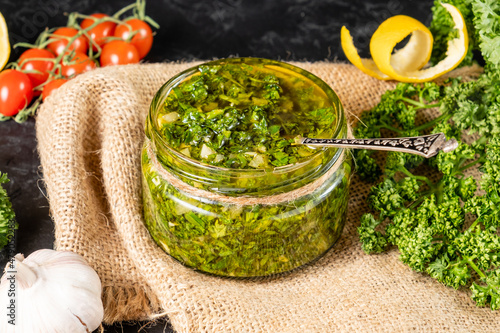 Delicious and healthy traditional sauce for chimichurri meat in a glass jar with a spoon. photo