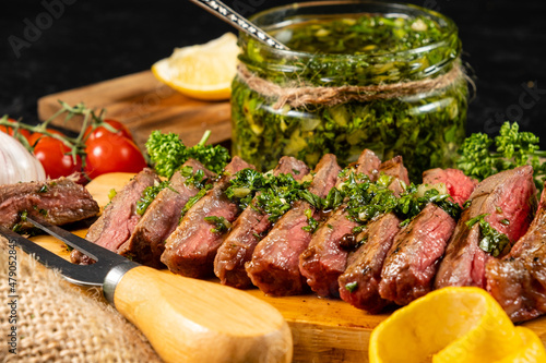 Close-up sliced steak drenched in green chimichurri sauce, selective focus.