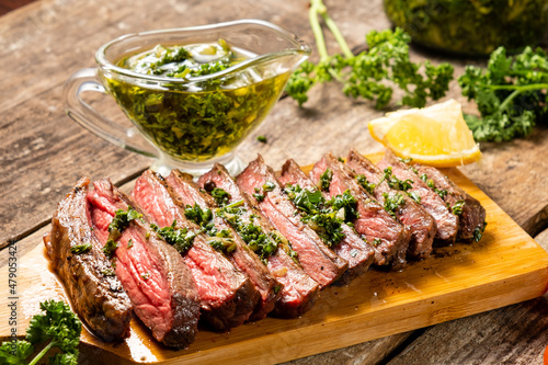 Appetizing beef steak cooked and sliced on a wooden table with chimichurri sauce.