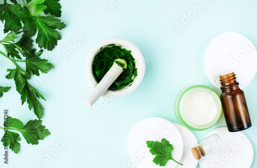 Botanical cosmetic product top view fresh green parsley plant leaves mashed for facial mask on light blue background, herbal skin care and organic beauty treatment homemade recipe