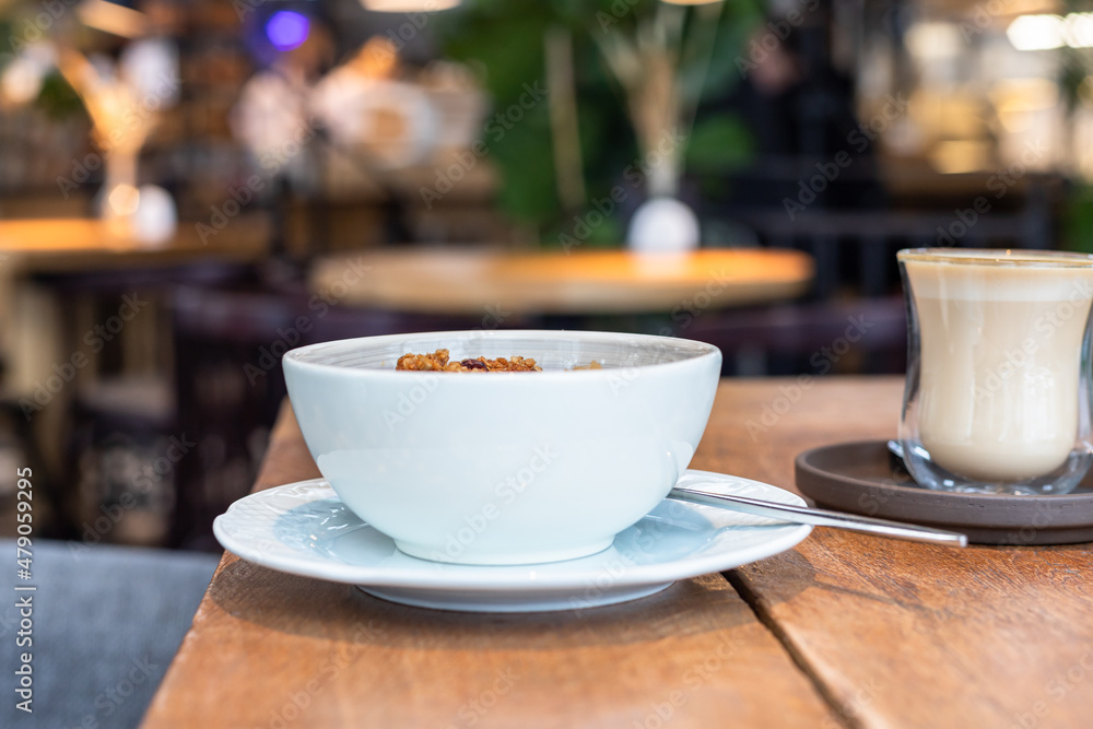 Composition with a bowl of oatmeal and a cup of cappuccino on wooden table, blurred cafe background. Healthy and tasty breakfast with oatmeal porridge. Composition with a bowl of oatmeal and a cup of cappuccino on wooden table, blurred cafe background. Healthy and tasty breakfast with oatmeal porridge.