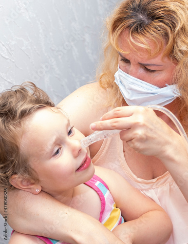 A Caucasian family  a woman cleans the nose of a child. A 4-year-old girl has a cold virus.