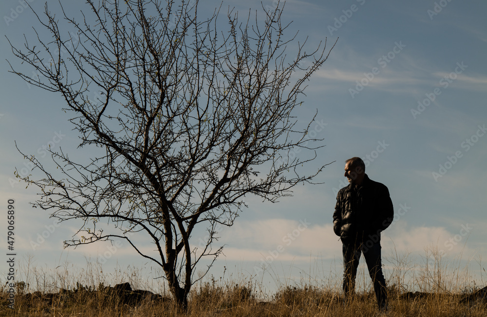 Portrait of adult man in winter clothes standing on fields with bare tree against blue sky Portrait of adult man in winter clothes standing on fields with bare tree against blue sky