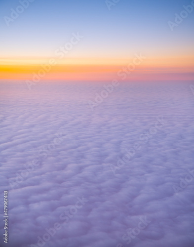 view of sea of clouds at sunset out of airplane window seat window orange sunset with pink and purple fluffy clouds as seen while in flight on airplane our of plane window heavenly horizontal format 