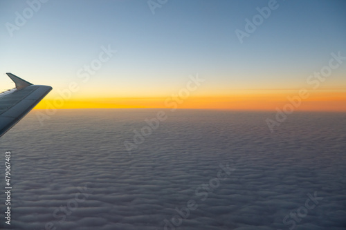 view of sea of clouds at sunset out of airplane window seat window orange sunset with pink and purple fluffy clouds as seen while in flight on airplane our of plane window heavenly horizontal format 