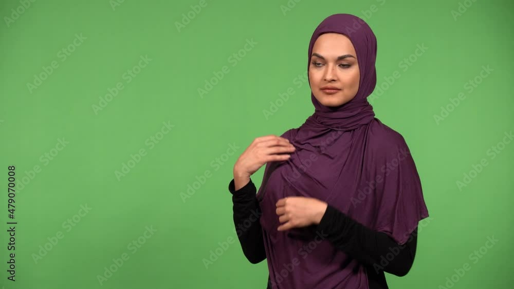 A young beautiful Muslim woman adjusts her clothes and smiles at the camera - green screen background A young beautiful Muslim woman adjusts her clothes and smiles at the camera - green screen background
