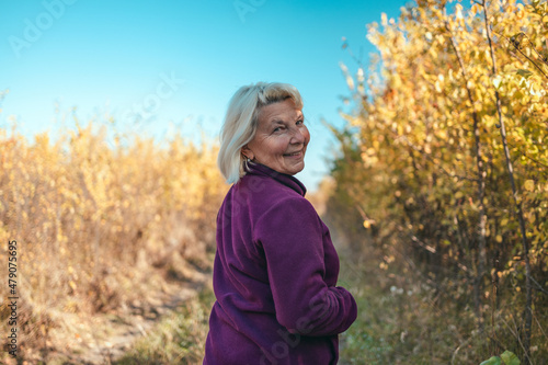 Portrait of a happy active beautiful senior woman running outdoors in the autumn forest in the morning