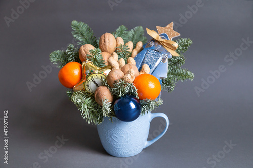Fototapeta Naklejka Na Ścianę i Meble -  Food floristry. Christmas edible bouquet with nuts, tangerines, nobilis and christmas decor in a blue cup on a gray background