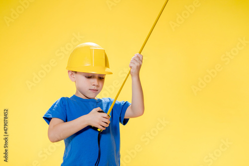 A little boy in a protective construction helmet measures with a tape measure