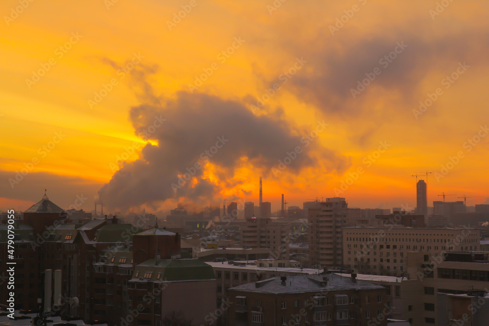 Cityscape with fiery yellow dawn and picturesque smoke from the thermal power plant pipes.
