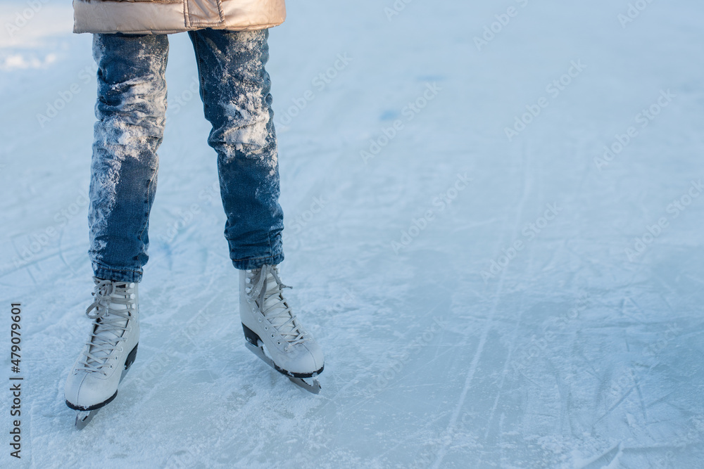 little girl in jeans in white figure skates is skating on the rink, winter fun and games, an open-air ice rink little girl in jeans in white figure skates is skating on the rink, winter fun and games, an open-air ice rink