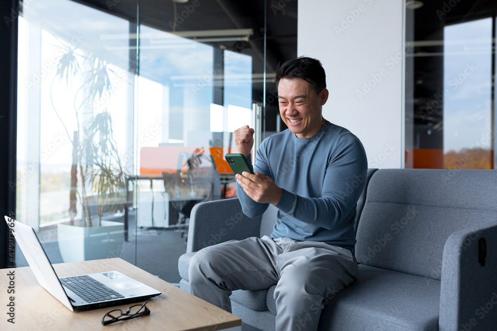 Close-up photo of male businessman using phone in modern office, asian looking at phone display and smiling, online call