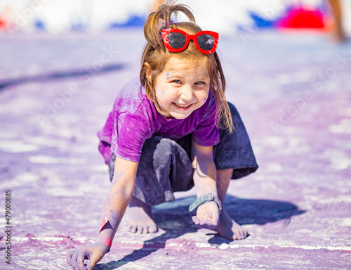 a little, cheerful girl at the Holi festival, in a purple T-shirt, stained with paint
