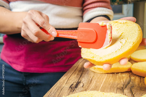 A woman spreads mayonnaise on a hamburger bun with sesame seeds. photo