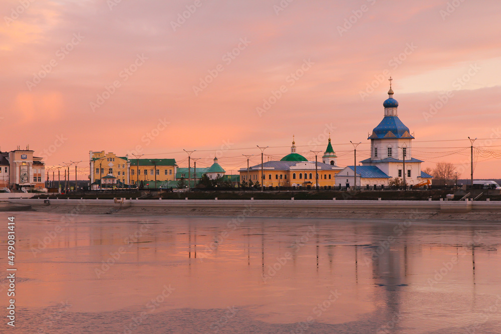 Colourful and bright sunrise in the Volga river embankment in Cheboksay city with a view of the church, monastery, old buildings and its reflections in the water.