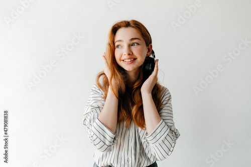 Portrait of happy redhead woman listening to music using black wireless headphones. Attractive smiling happy woman in stylish outfit, having fun