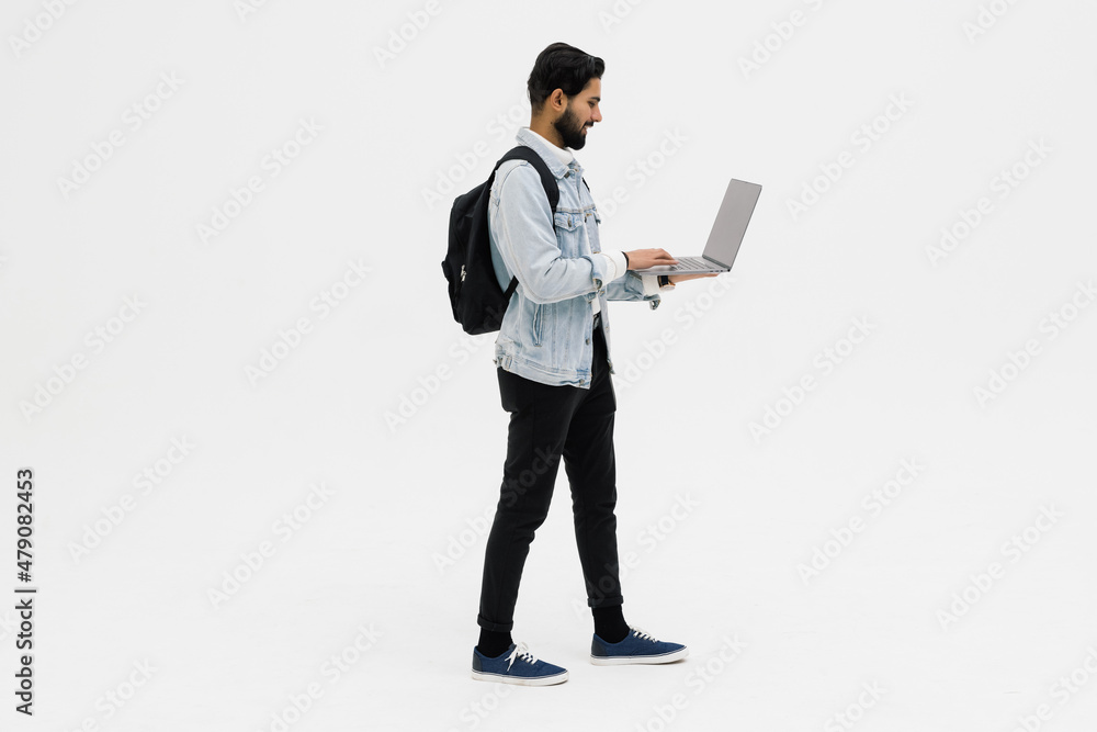 Indian handsome young man with backpack standing and using laptop Indian handsome young man with backpack standing and using laptop