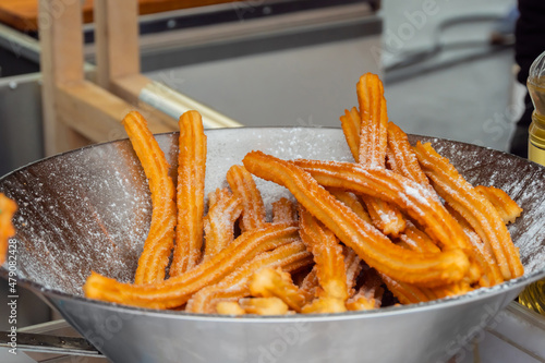 Homemade crunchy churros in steel bowl at summer outdoor food market - close up view. Traditional Spanich cuisine, catering, cookery, gastronomy and street food concept photo