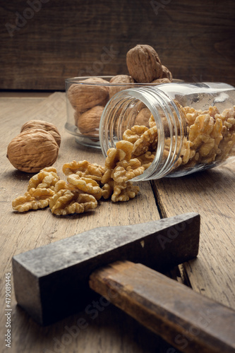 Nuts coming out of a glass jar and hammer on a wooden table in a dark environment.. High quality photo