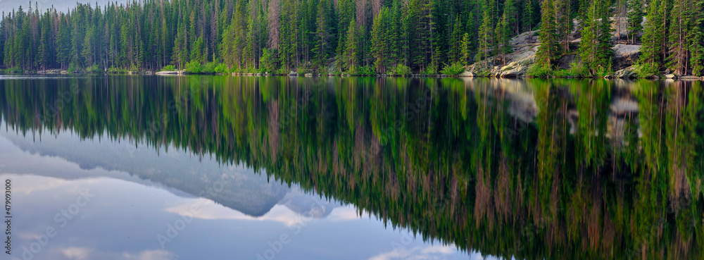 Panoramic image of Pine trees and mountains reflected in the calm waters of Bear lake in Rocky Mountain National Park Colorado