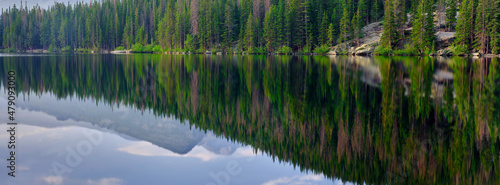 Panoramic image of Pine trees and mountains reflected in the calm waters of Bear lake in Rocky Mountain National Park Colorado