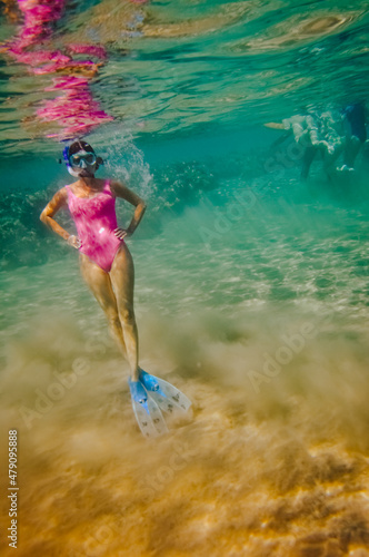 a girl in a pink swimsuit in a mask and fins swims underwater