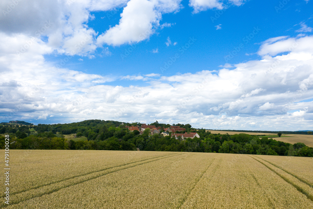 A wheat field stretches out in front of a traditional French village in Europe, France, Burgundy, Nievre, in summer on a sunny day. A wheat field stretches out in front of a traditional French village in Europe, France, Burgundy, Nievre, in summer on a sunny day.