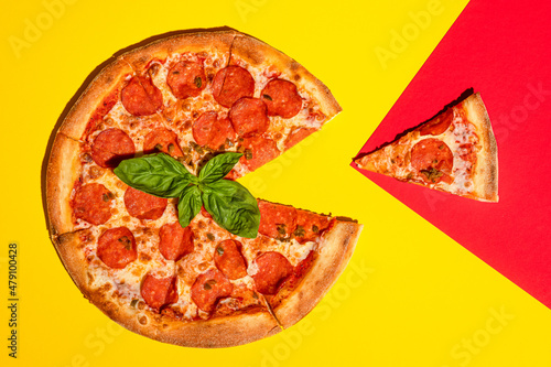 Pepperoni pizza on a colored yellow-red background with basil