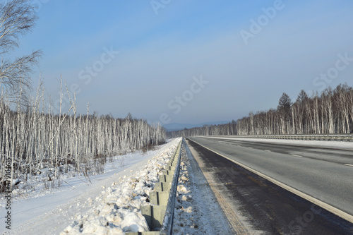 Paved road among birch trees. Winter. Snow on the roadside and in the woods.