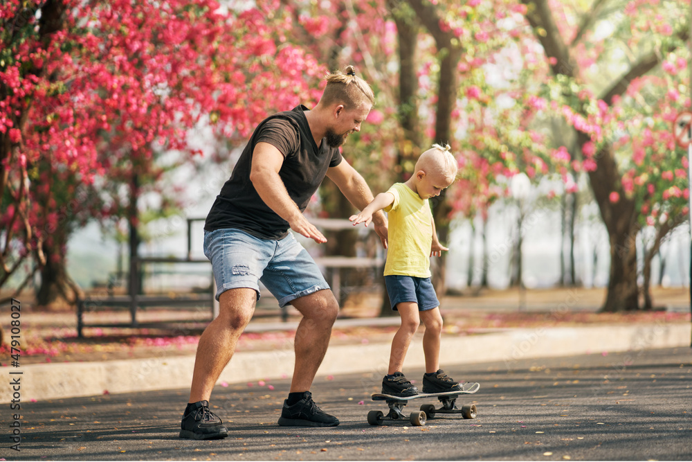 Fototapeta premium Father training his son to ride a skateboard in park on spring time.