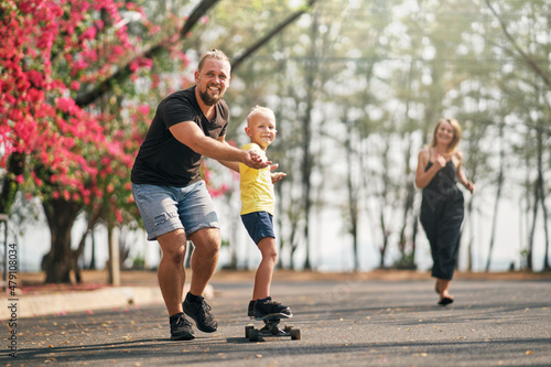 Father training his son to ride a skateboard in park on spring time.