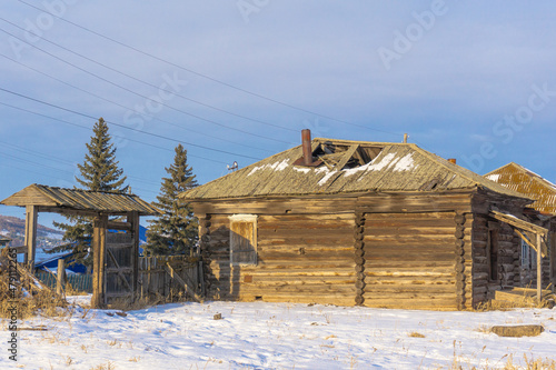 Canvas Print A dilapidated uninhabited dilapidated old wooden house built of logs with a collapsed roof from old age, a fallen fence, in winter