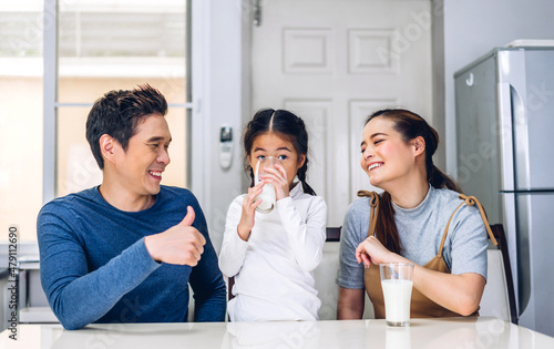 Portrait of enjoy happy love asian family father and mother with little asian girl smiling and having protein breakfast drinking and hold glasses of milk at table in kitchen