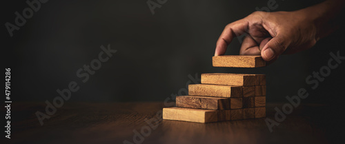 Fotografia Close-up hand is placing wood block tower stacked in stair step with caution to prevent collapse or crash concepts of financial risk management and strategic planning