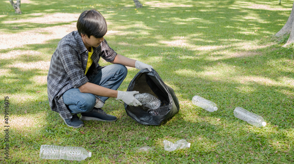 Fototapeta premium young Asian men, garbage collection pick up plastic bottles, put garbage in black garbage bags to clean up at parks, avoid pollution, be friendly to the environment and ecosystem