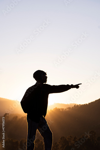 Silhouette of a young boy standing in the fields and the beautiful mountains in the background captured during sunset.