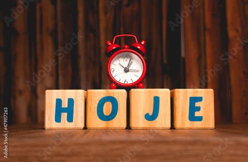 A palavra hoje escrita em Português do Brasil em blocos de madeira com um relógio vermelho com fundo amadeirado. Tempo de começar, construir e conquistar. Motivação.  photo