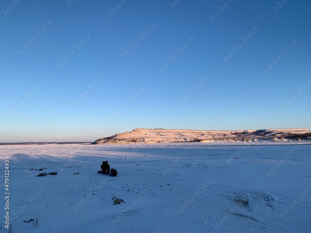 a snowmobile in the distance driving on a frozen river in the snow against the background of the hills lit by the sunset a snowmobile in the distance driving on a frozen river in the snow against the background of the hills lit by the sunset