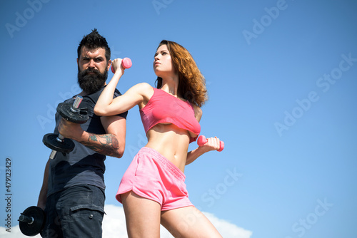 Fit couple doing exercising outdoors with dumbbell. Healthy lifestyle concept, sport. Sexy couple exercising with dumbbells. Strong man and sexy woman working out with dumbbells on sky background.