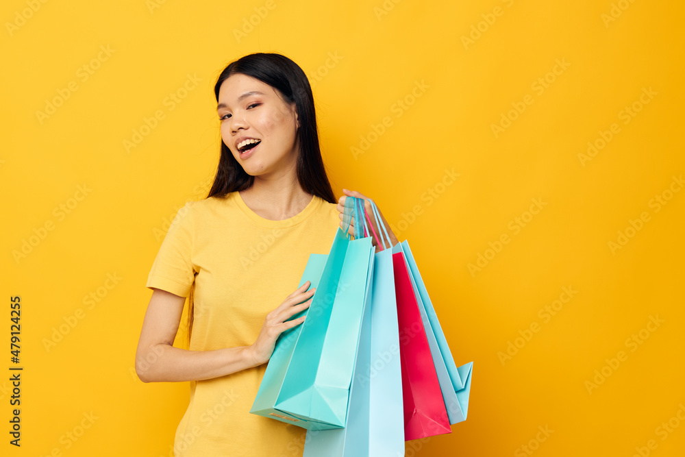 Charming young Asian woman in a yellow T-shirt with multicolored shopping bags studio model unaltered Charming young Asian woman in a yellow T-shirt with multicolored shopping bags studio model unaltered