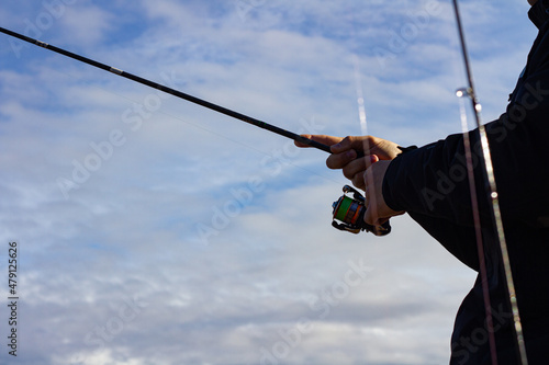 Hand with a fishing rod. Fisherman with a fishing rod. Close-up is a hand holding a spinning rod. Colorful view, blurred background, selective focus.