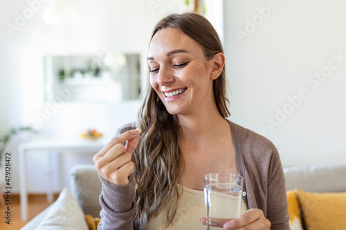 Head shot portrait happy woman holds pill glass of water, takes daily medicine vitamin D, omega 3 supplements, skin hair nail strengthen and beauty, medication for health care concept photo