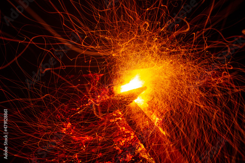 Fire sparks. Burning firewood at night. Bonfire in a tourist camp outdoors in the mountains. Flame and fire sparks on a dark abstract background. Fuel, energy and energy