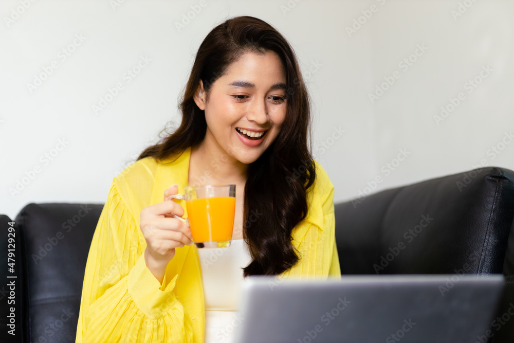 Lovely Asian black hair woman sitting, using laptop computer and drinking orange juice on bed in living room. Lovely Asian black hair woman sitting, using laptop computer and drinking orange juice on bed in living room.