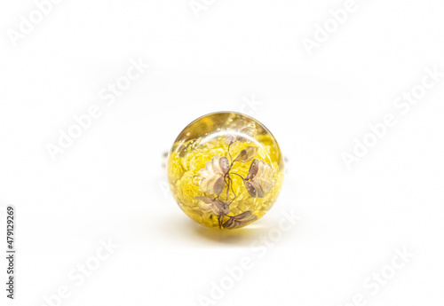 Sphere resin ball with plants inside. Yellow immortelle flowers and and brown briza media plants in jewelry. Selective focus on the details  blurred background.